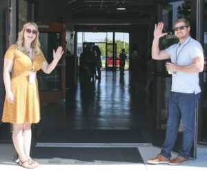 two employees waving at an entrance with badges on lanyards